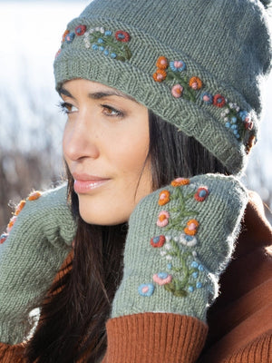 Woman wearing a green knitted hat and mittens with floral patterns outdoors.